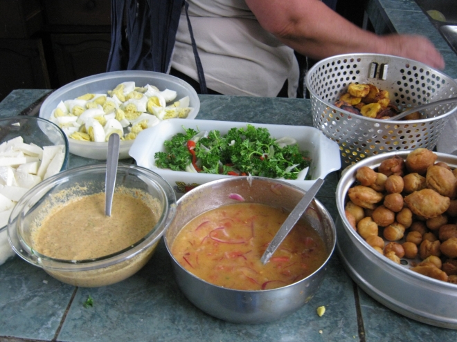 Adornos (decorations) for the fanesca. (Front to back, left to right) Cheese, squash-seed chili sauce, hot sauce, fritos (empanadas, dough balls). Hard boiled eggs; finely sliced red chili pepper, parsley, cebolla blanca; fried maduro (ripe plantain). photo © Lorraine Caputo 